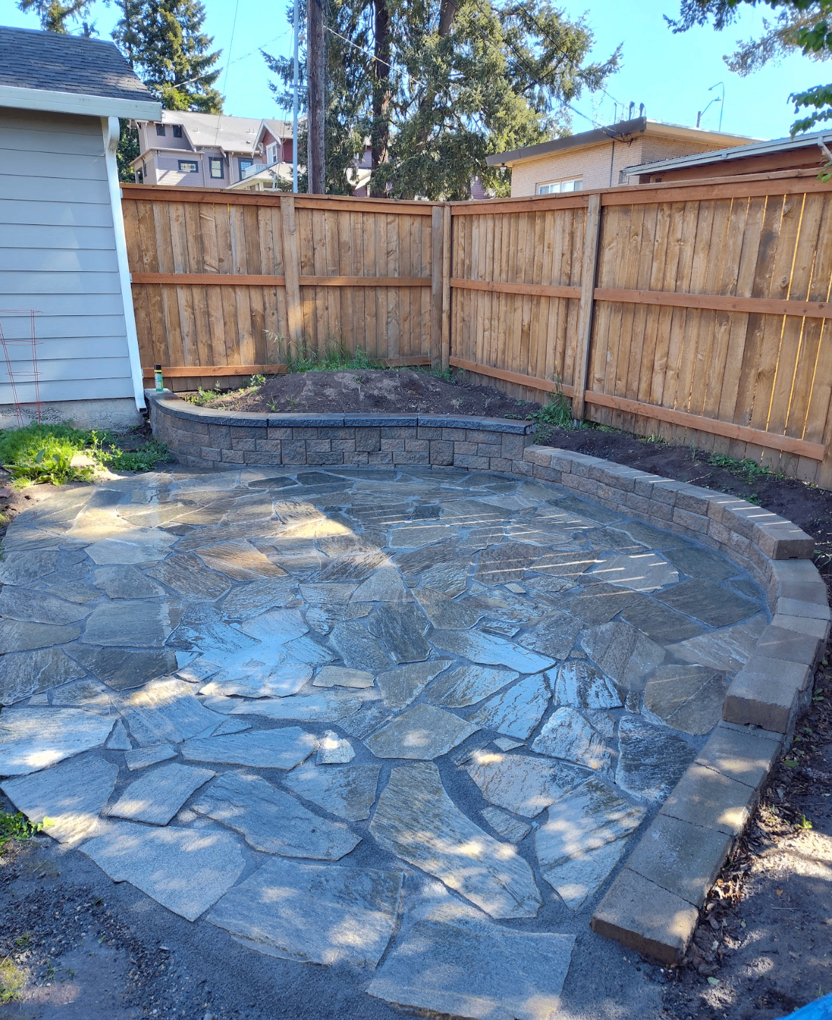 Custom curved flagstone patio with retaining wall seating area in a fenced backyard