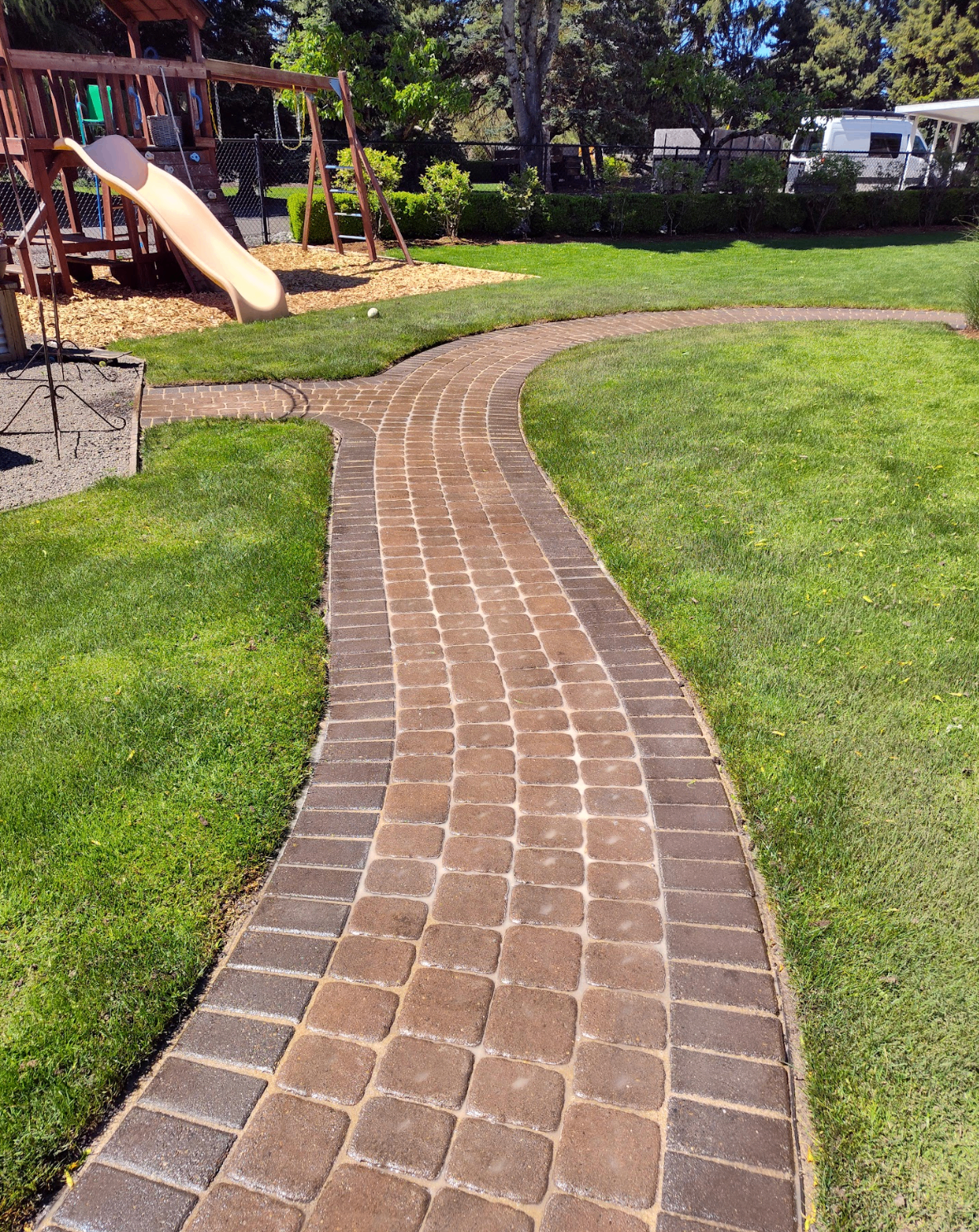 Curved tumbled paver walkway winding through a green backyard lawn