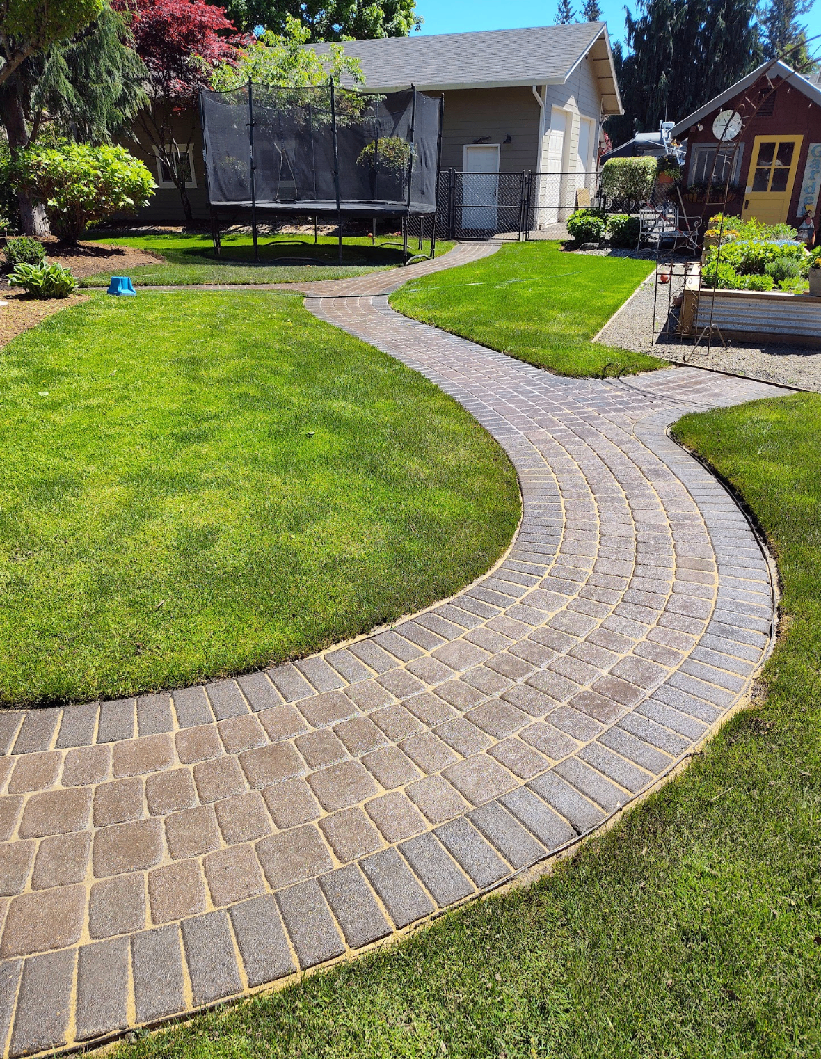 Long winding paver pathway connecting backyard lawn areas to garage and garden